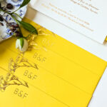 Enveloppes jaune vif personnalisées avec fleurs d’achillée et initiales des mariés en dorure or brillante