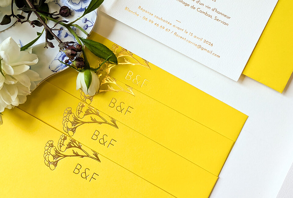 Enveloppes jaune vif personnalisées avec fleurs d’achillée et initiales des mariés en dorure or brillante