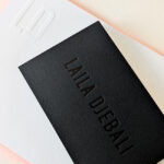 Carte de visite pour consultante avec marquage à chaud noir brillant sur papier noir mat texturé, accompagnée d’une carte de correspondance blanche avec logo débossé.
