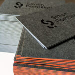 Cartes de visite haut de gamme pour architecte d’intérieur, avec marquage à chaud noir brillant sur papier anthracite mat et tranches orange et bleu clair.